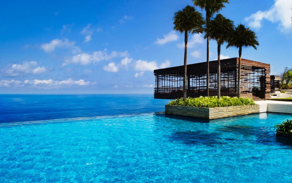  An infinity pool with a view of the ocean and a luxury hotel in the background.